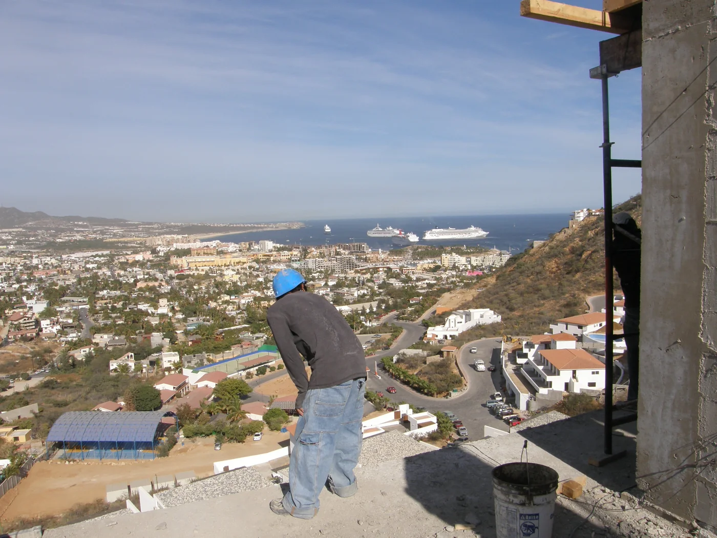 Worker on an unfinished terrace overlooking Cabo San Lucas and cruise ships